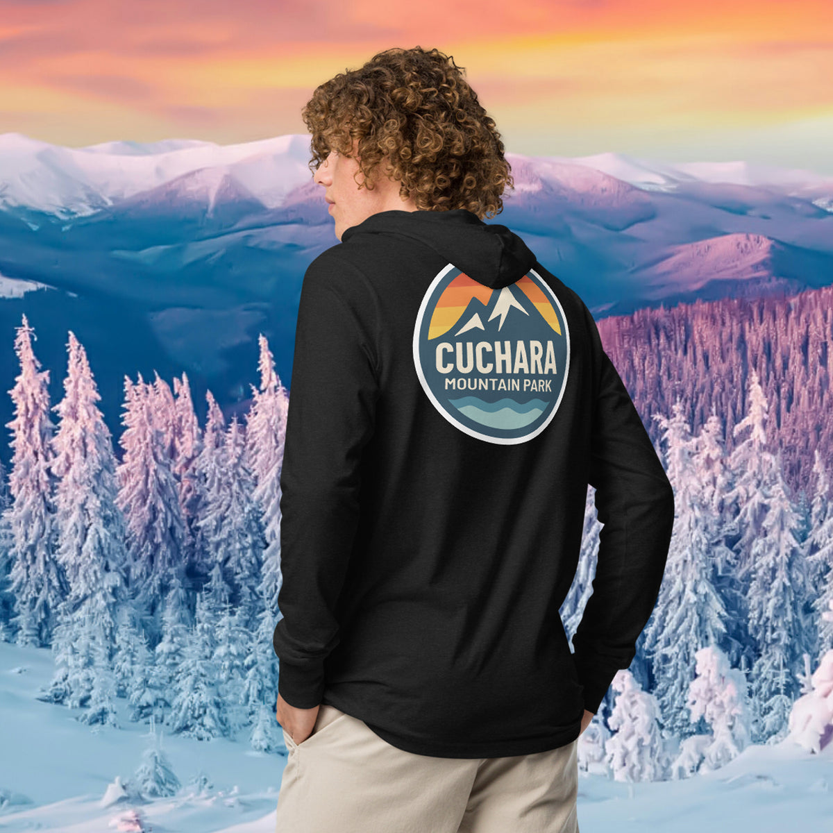Person wearing a black hoodie with 'Cuchara Mountain Park' logo in a snowy mountain landscape.  Person wearing a black hoodie with a logo against a snowy mountain landscape.  lightweight long-sleeve hooded tee, unrestricted movement shirt, all-season layering top, comfortable athletic fit, stylish outdoor outfit, year-round trail essential, men's hooded t-shirt, cuchara mountain park hoodie, cuchara mountain park long sleeve shirt
