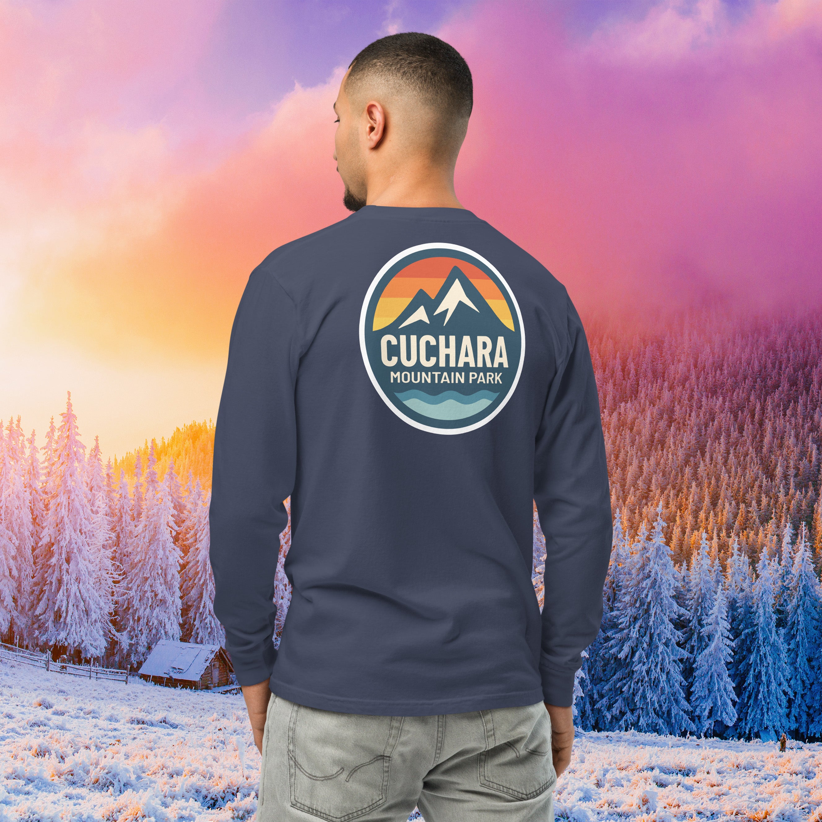 Man wearing a black long-sleeve shirt with a logo against a colorful winter landscape.  Built for endurance. This unisex heavyweight long sleeve is garment-dyed for a rugged, lived-in look. Pre-shrunk fabric ensures maximum durable comfort on every expedition. Cuchara Mountain Park clothing, cuchara long sleeve shirt