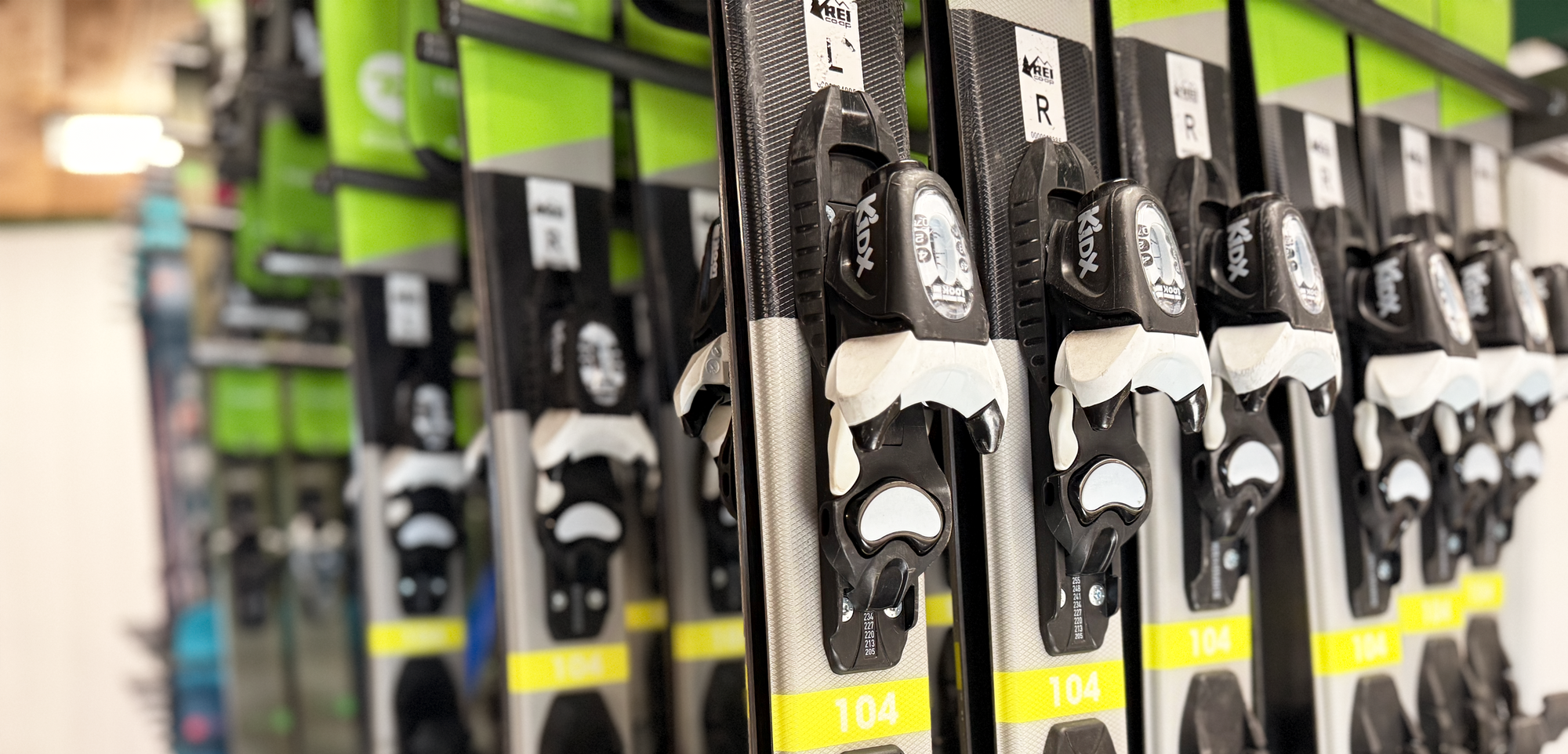 Row of skis with bindings on a rack in a store.  High-quality downhill ski packages for all skill levels.