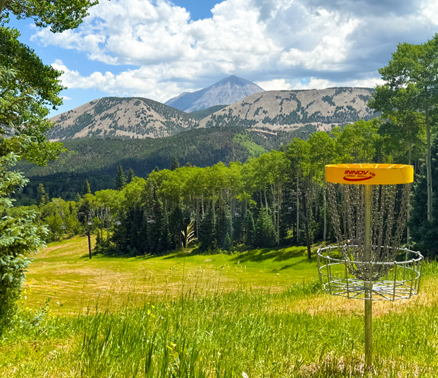 Disc golfer teeing off on the challenging 18-hole mountain course at Cuchara Mountain Park, showcasing a technical hole near the creek.  Cuchara Mountain Park disc golf course, 18-hole mountain course, disc golfer putting basket view,  high elevation disc golf challenge,  technical shots Lower Baker Creek, Colorado premier disc golf experience, affordable mountain disc golf,  find course on UDisc app
