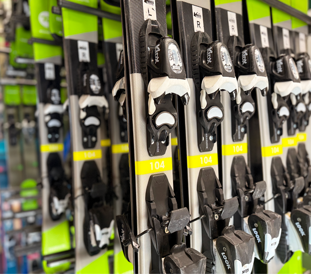 Row of skis with bindings on a rack in a store.  High-quality downhill ski packages for all skill levels.