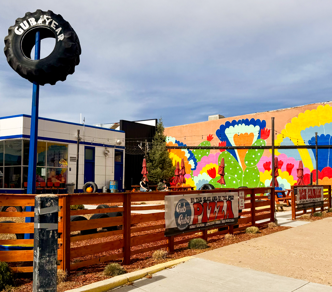 Colorful mural on a building with a tire sign and pizza restaurant sign in the foreground. gub gub in Walsenburg Colorado, walsenburg restaurants